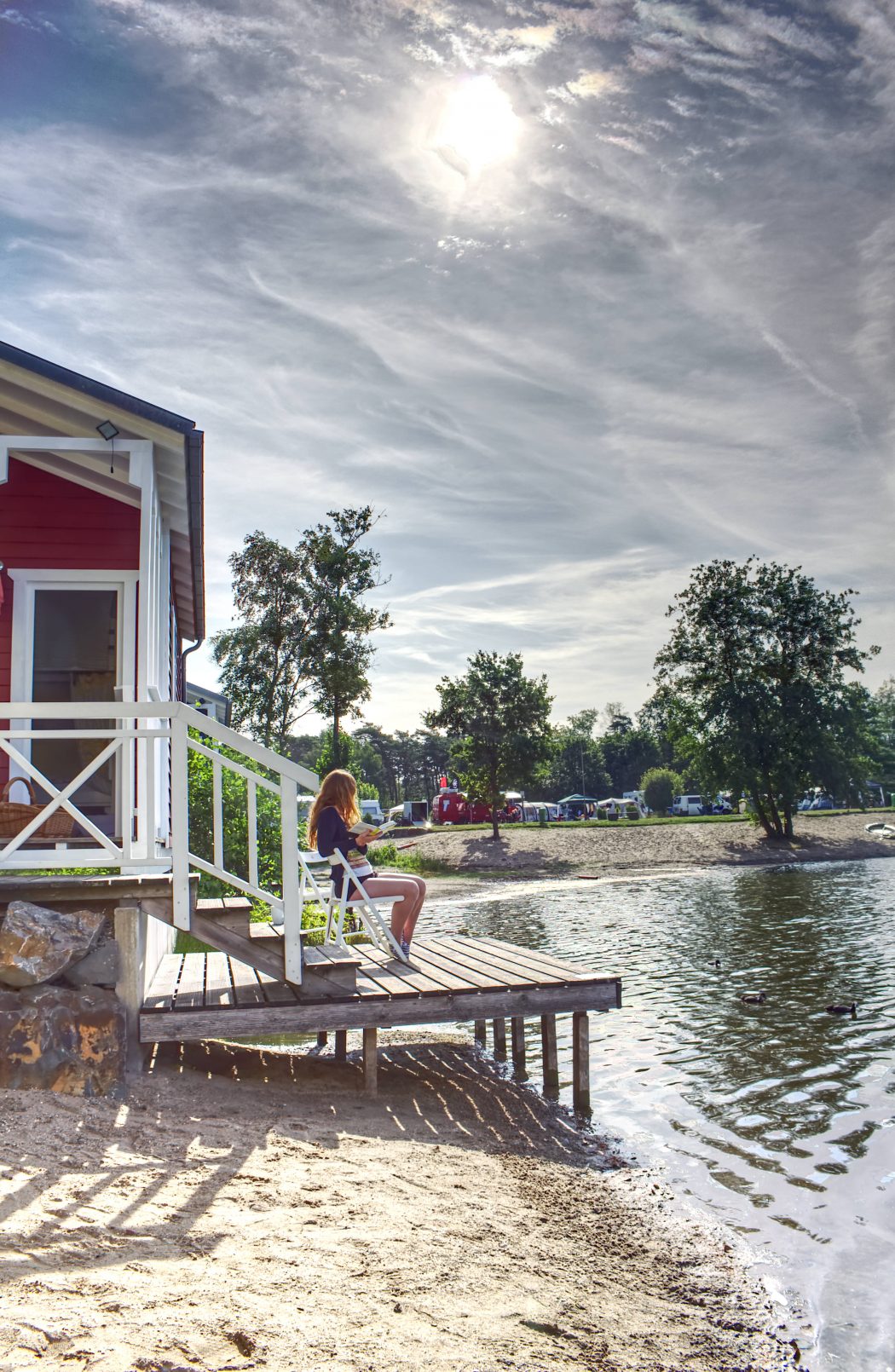 Das Foto zeigt eine Frau mit Buch vor einem Haus am See in der Dingdener Heide