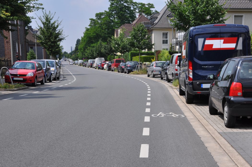 Das Foto zeigt einen schmalen Radweg auf einer Verkehrsstraße