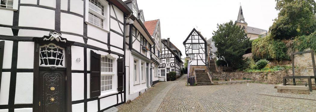 Das Foto zeigt traditionelle Fachwerkhäuser und eine moderne Brunneninstallation in Essen-Kettwig
