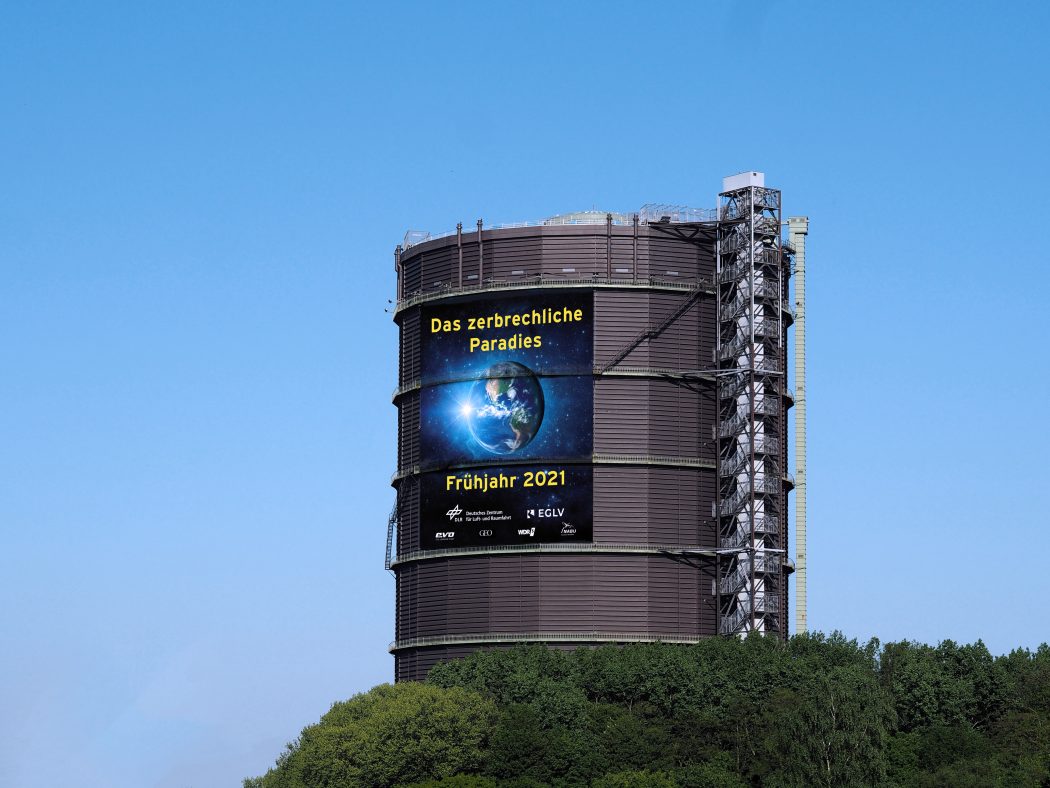 Das Foto zeigt eine Montage des Plakate der neuen Gasometer Ausstellung "Das zerbrechliche Paradies"