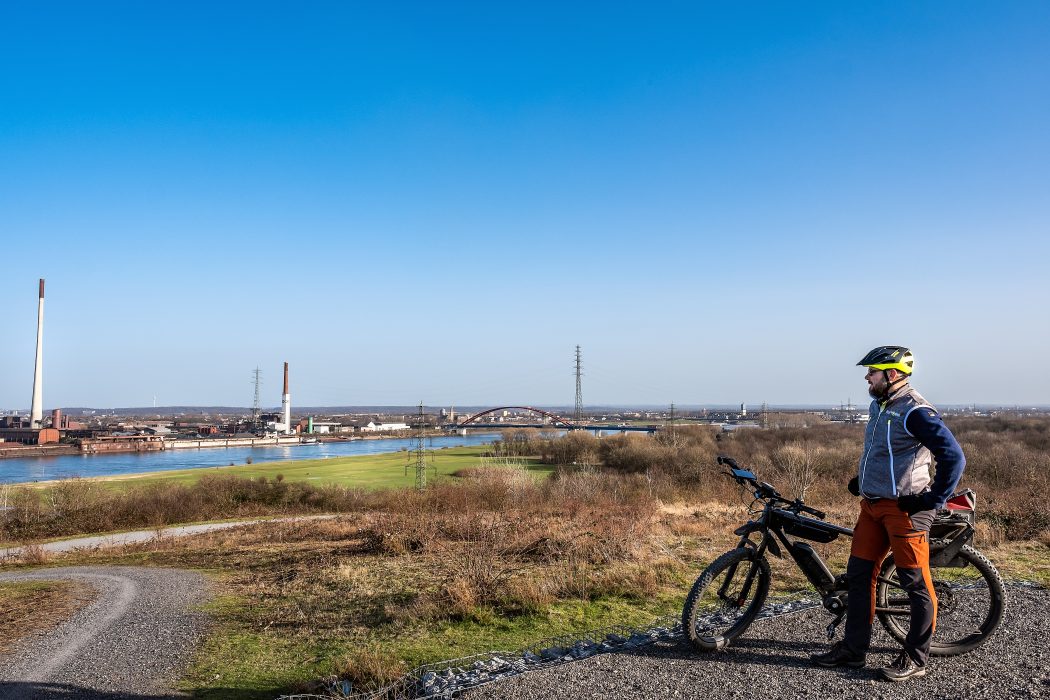 Das Foto zeigt einen Radfahrer auf dem Rockelsberg mit Aussicht auf den Rhein bei Duisburg