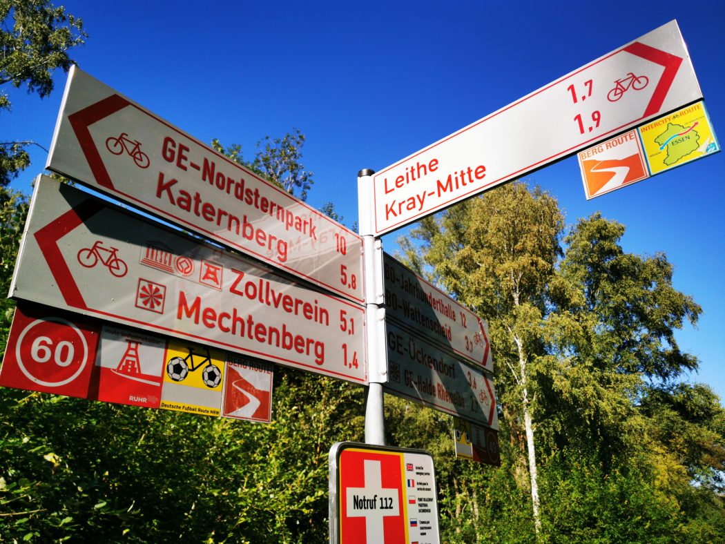 Das Foto zeigt einen typischen Pfeilwegweiser mit Themenrouten und Knotenpunkteinschub