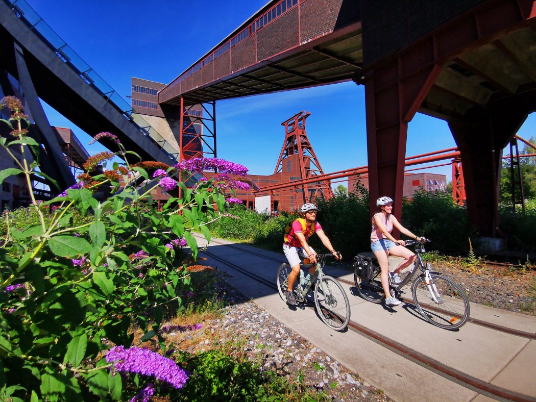 Das Foto zeigt zwei Radfahrer auf der Route Industriekultur per Rad auf dem Gelände der Zeche Zollverein in Essen