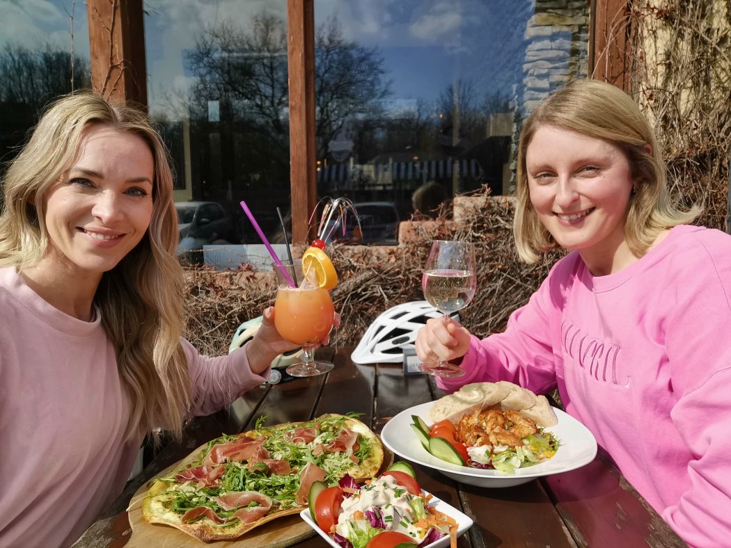 Das Foto zeigt Sandra und Katalina mit Flammkuchen, Salat zu Cocktail und Weißweinschorle im Herzblut an der Grafenmühle in Bottrop