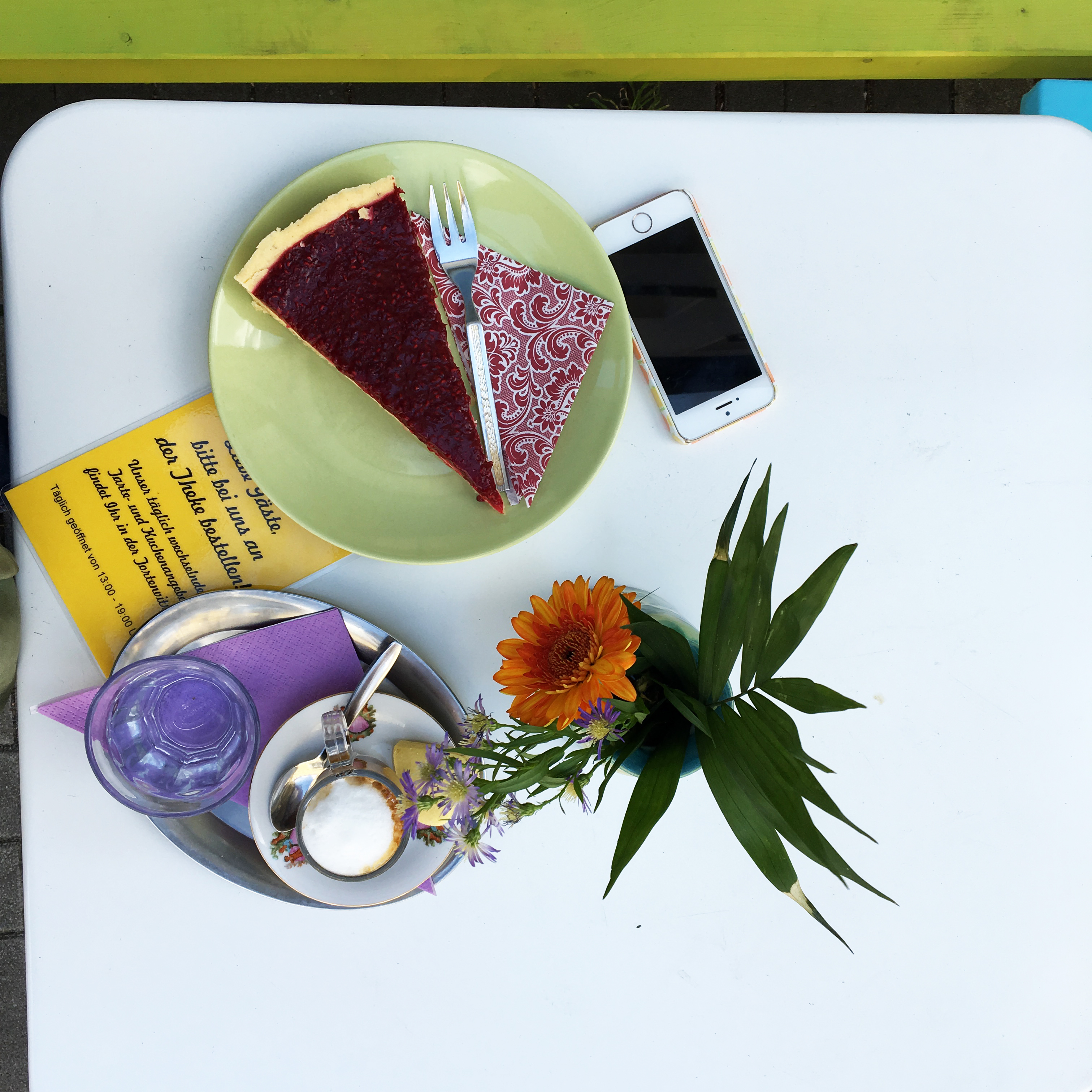 Das Foto zeigt ein Stück Kuchen, einen Espresso Macchiato, ein Blümchen und ein Handy im Café Fräulein Coffea in Bochum-Ehrenfeld.