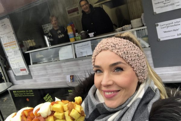 Das Foto zeigt die Blogautorin Sandra mit ihrer Currywurst am Stiel