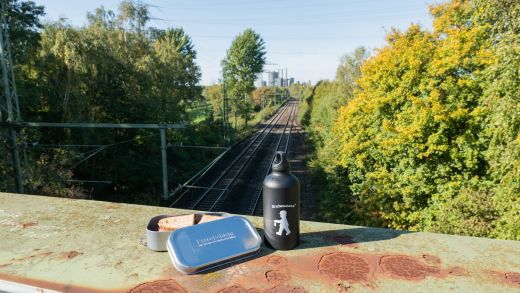 Das Bild zeigt ein Butterbrot und eine Trinkflasche auf einer Eisenbahnbrücke