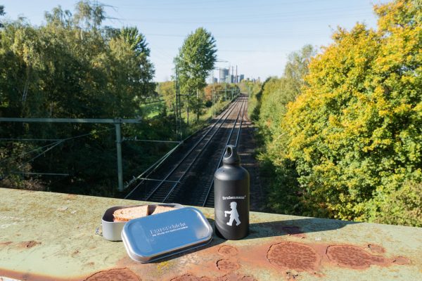 Das Bild zeigt ein Butterbrot und eine Trinkflasche auf einer Eisenbahnbrücke