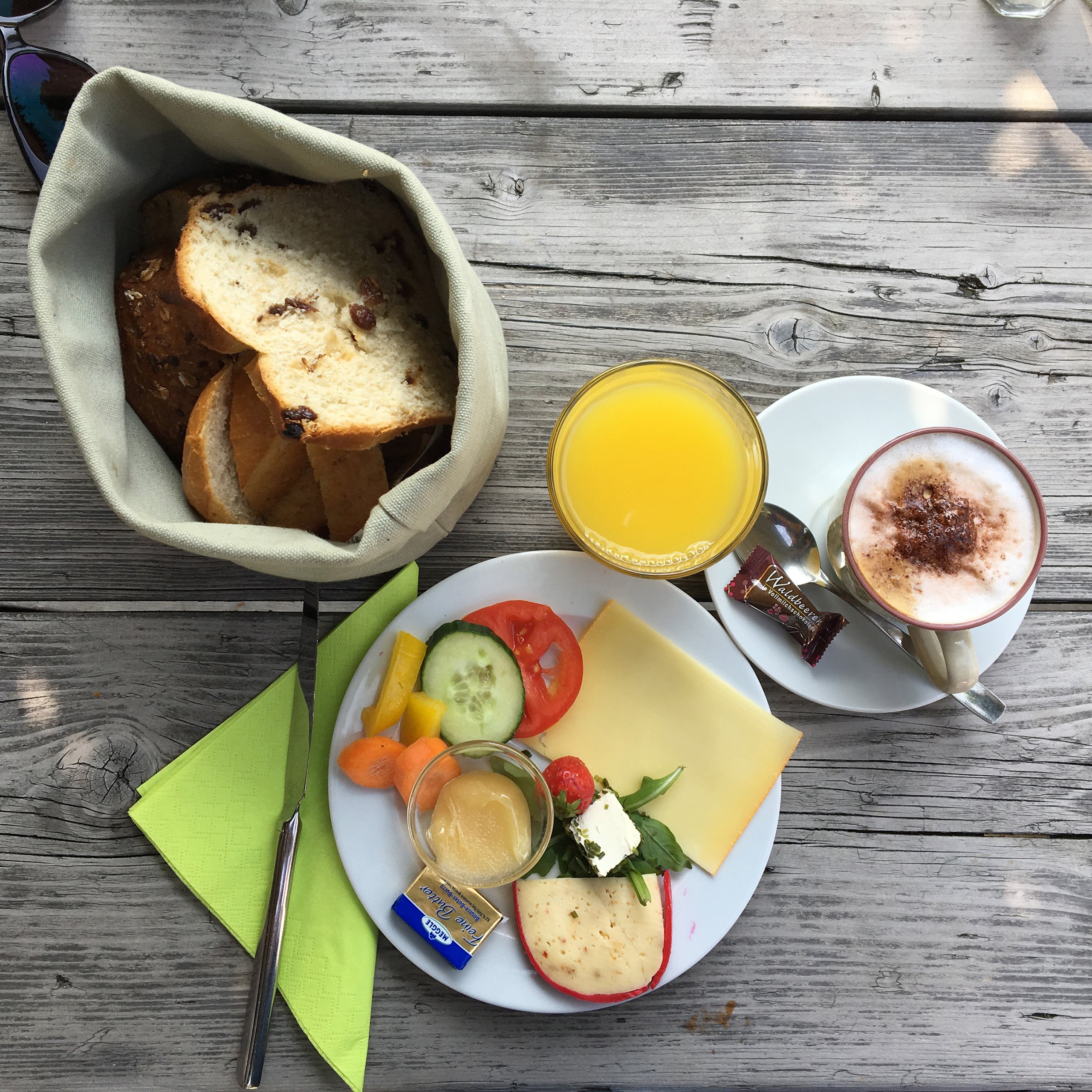 Das Bild zeigt einen gefüllten Frühstücksteller mit Capuccino und Brot