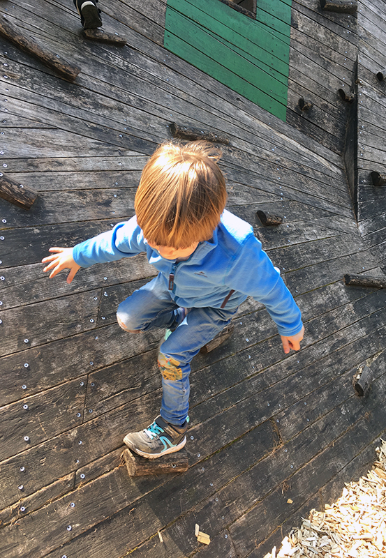 Das Bild zeigt einen kleinen Jungen beim Klettern an einer Holzwand im Kettelerhof in Haltern