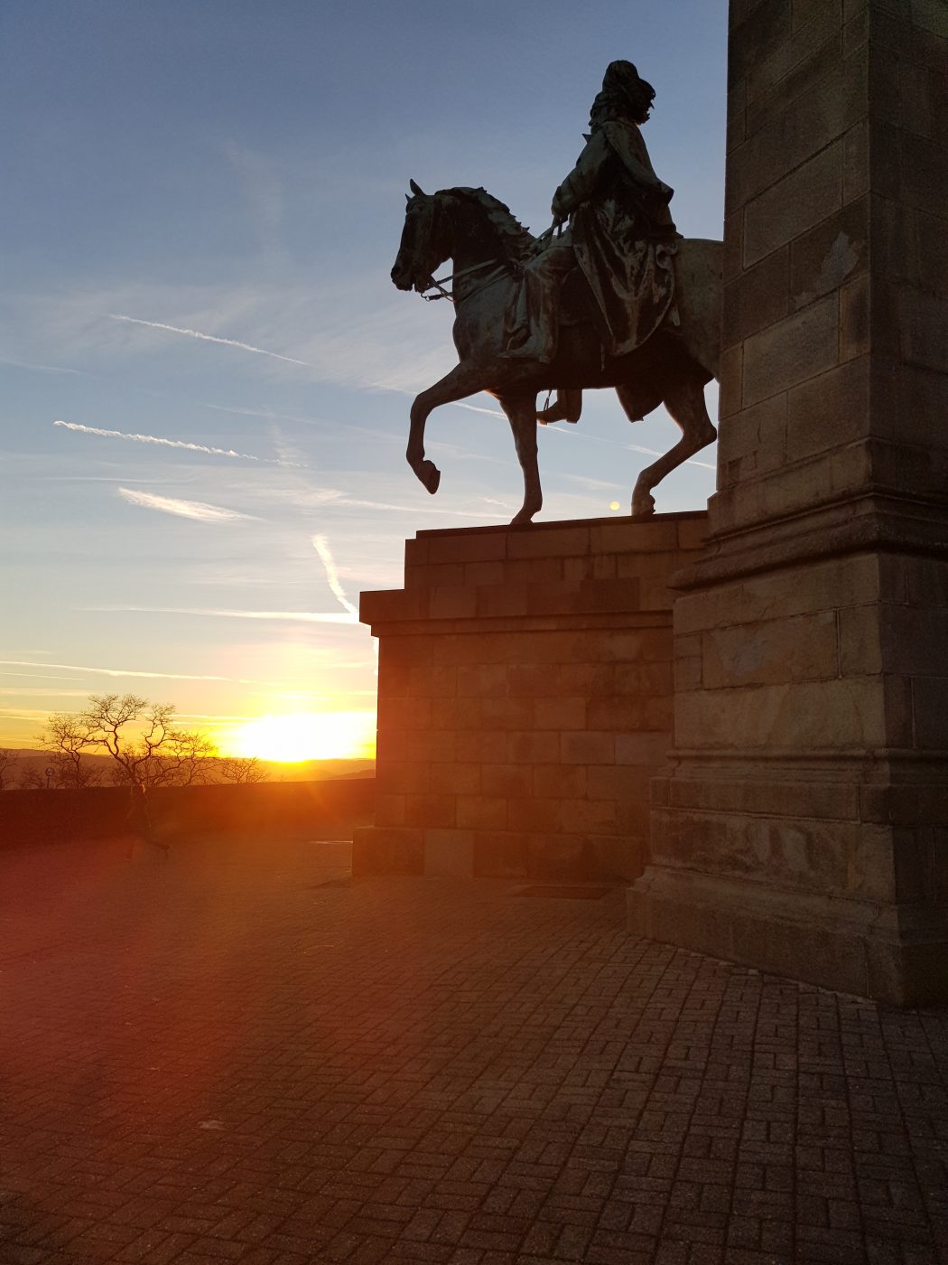 Das Bild zeigt eine Reiterstatue vor untergehender Sonne