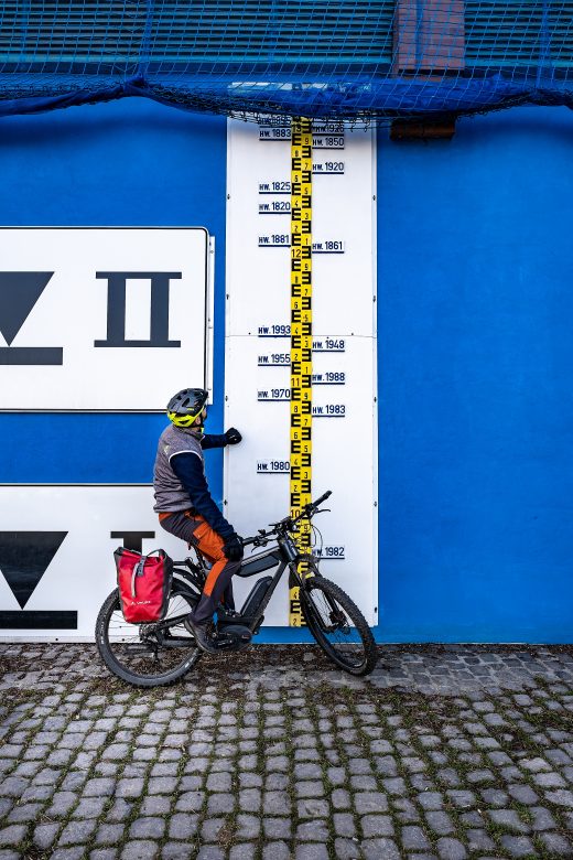 Das Foto zeigt einen Radfahrer an den Hochwassermarkierungen des Rheins in Duisburg