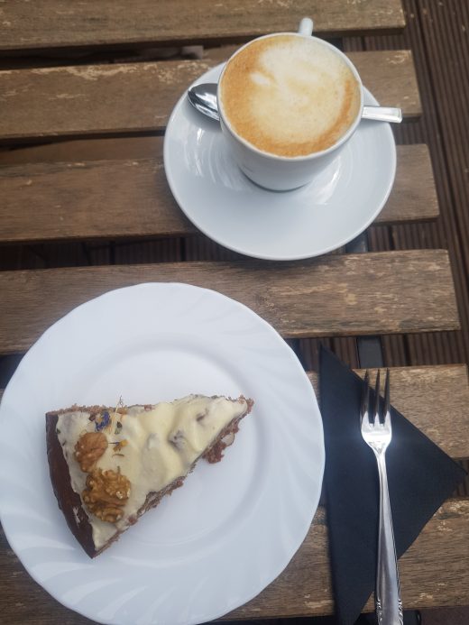 Das Foto zeigt Kuchen und Cappuccino im Hinterhof des Cafés Omi backt in Bochum Ehrenfeld
