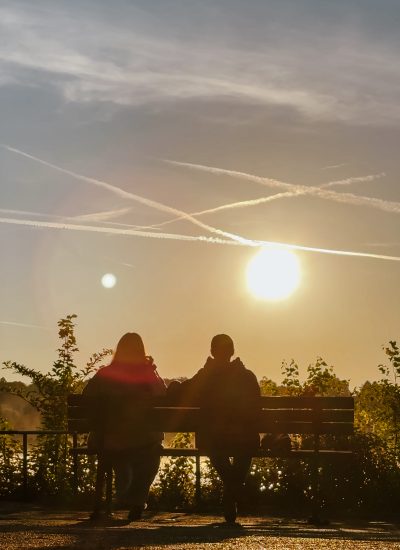 Eine Gruppe von Menschen sitzt auf einer Bank und schaut in die Sonne.