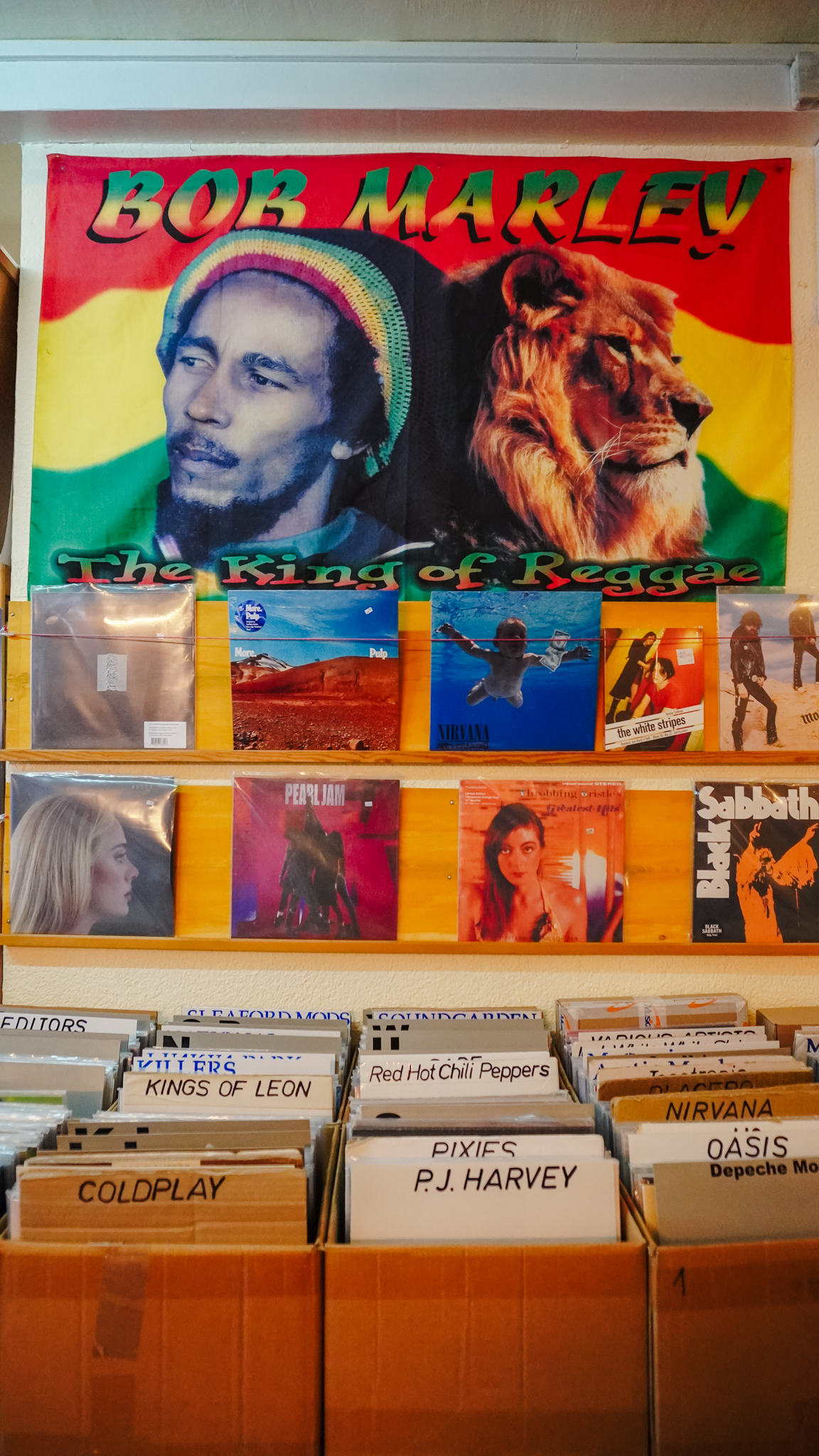Die Auslage eines Plattenladens mit einem bunten Bob Marley: The King of Reggae" über Regalen mit Vinylplatten von Künstlern wie Nirvana, Pearl Jam, Black Sabbath und Coldplay.