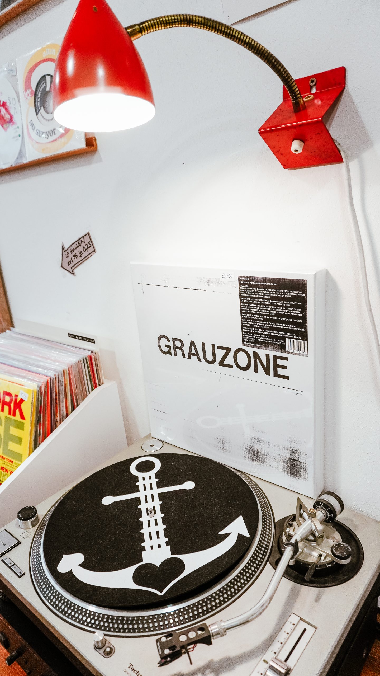 Unter einer roten Lampe steht ein Plattenspieler mit einer schwarzen Unterlage, auf der ein weißer Anker und ein Herz abgebildet sind. Eine Schallplatte mit dem Titel Grauzone steht aufrecht hinter dem Plattenteller, links sind weitere Platten zu sehen.